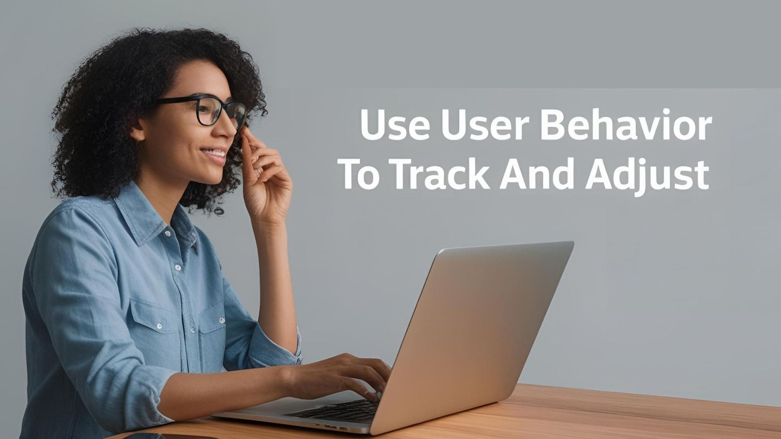 A person in a blue button-up shirt sits at a wooden table using a laptop, holding a pen while analyzing data. The image includes a text overlay stating 'Use User Behavior To Track And Adjust,' emphasizing the importance of tracking user behavior for optimization.